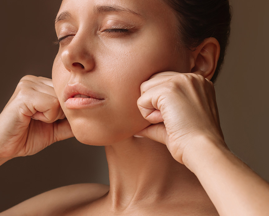 Young woman touching face with hands massaging her jaw isolated on a dark brown background.
