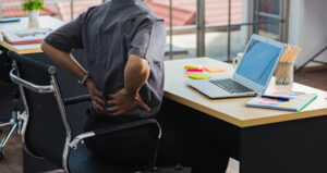 Man stretching his back in pain while sitting at the computer.