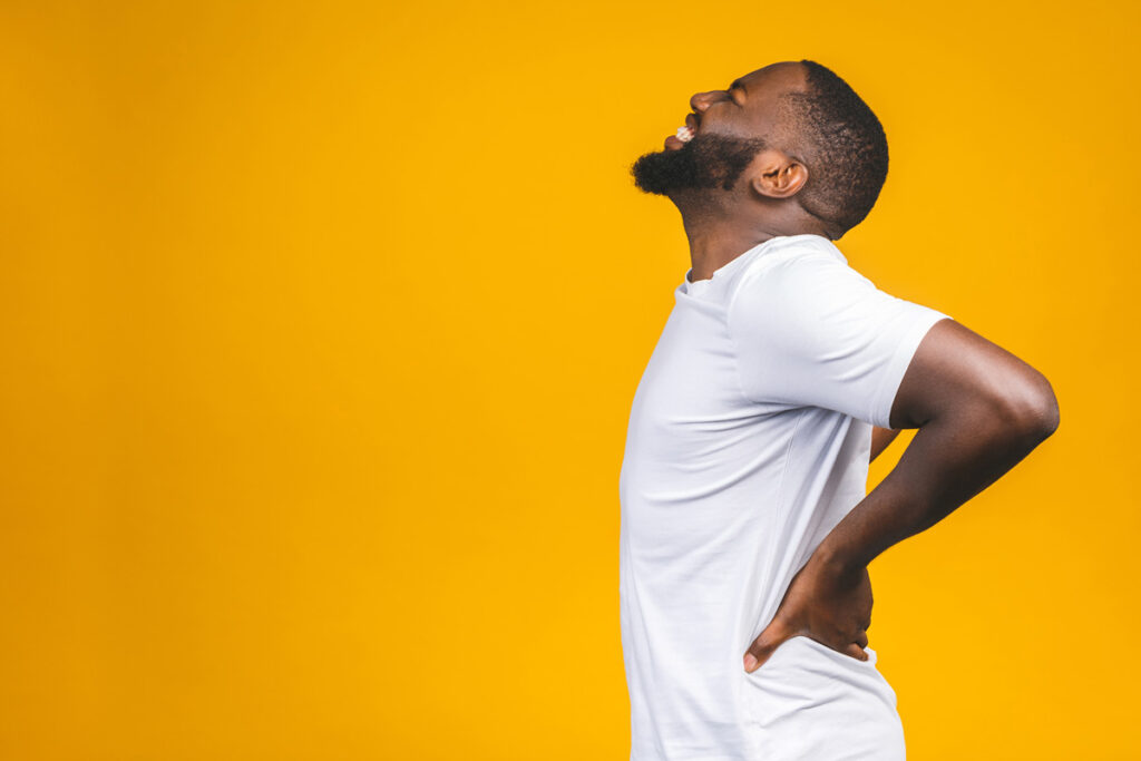 A man grabbing his back in pain in front of a yellow background in Bethesda.